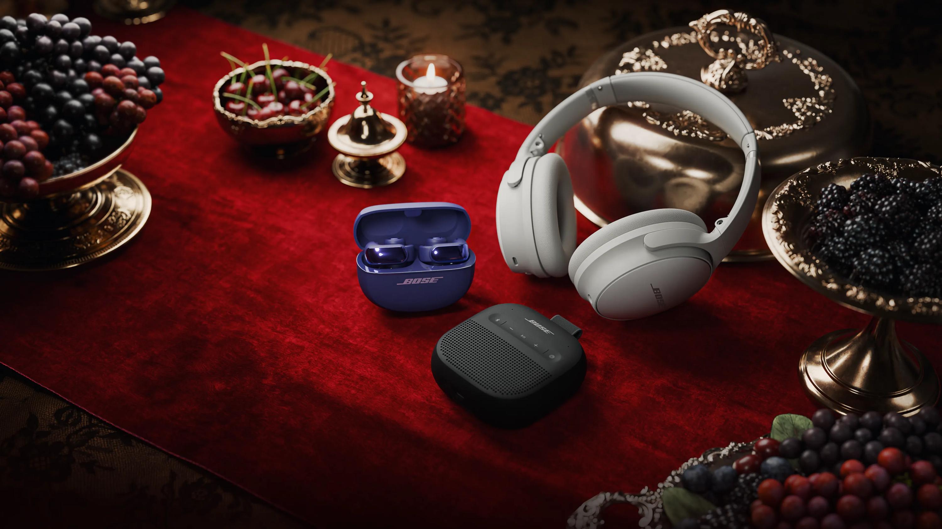 Bose Ultra Open Earbuds, SoundLink Portable Speaker (2nd Gen), and QuietComfort Headphones on a table decorated for the holidays.