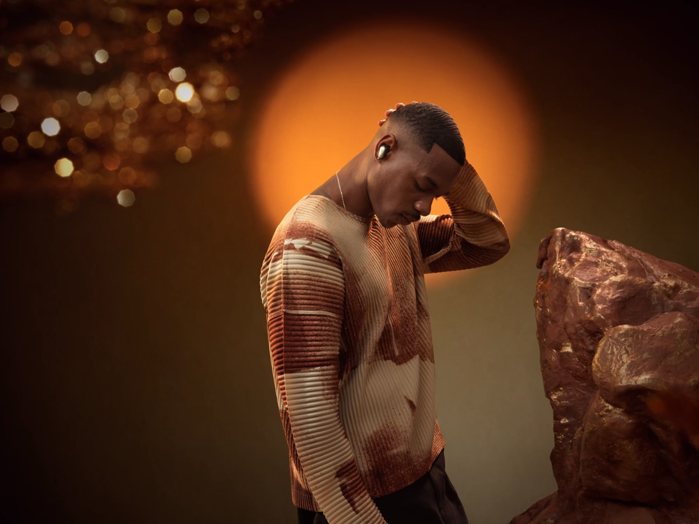 Man wearing Black QuietComfort Ultra Earbuds (2nd Gen) with an orange halo in the background.