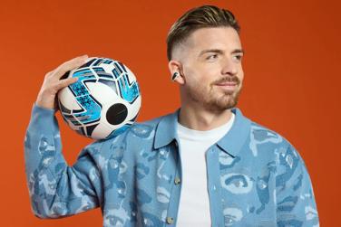 Jack Grealish wearing Bose Ultra Open Earbuds while holding a soccer ball