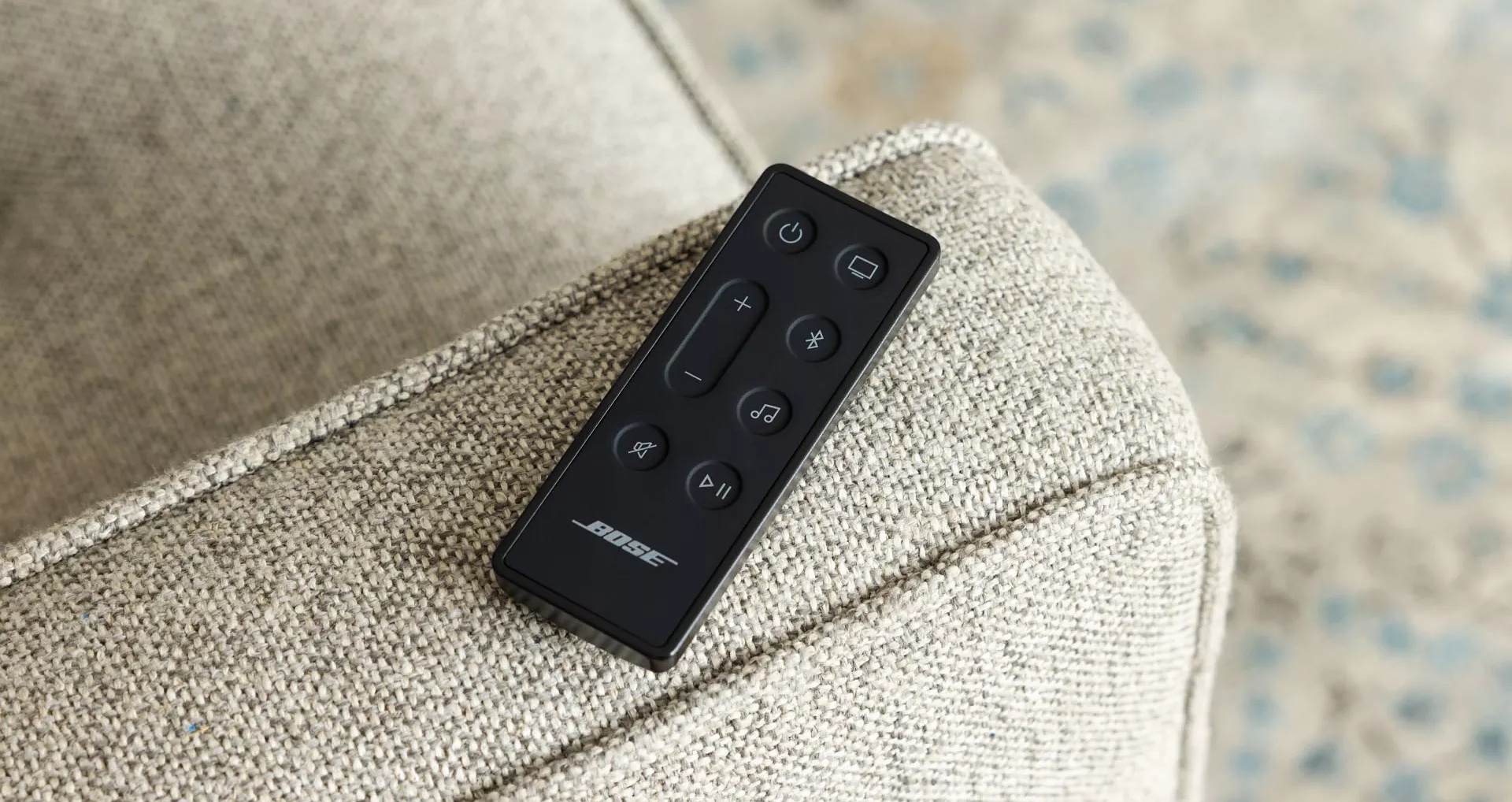 Télécommande de la barre de son Bose Smart Soundbar 600 sur le bras d’un canapé.