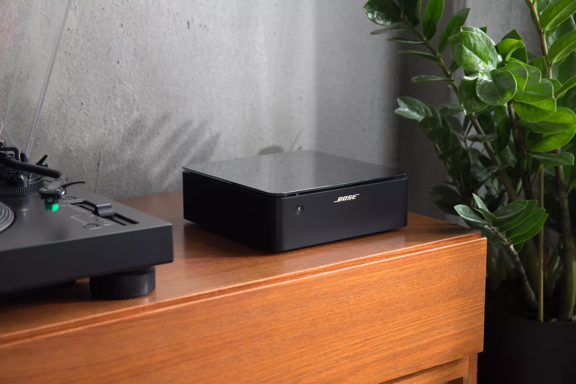 Bose Music Amplifier resting on table next to vinyl record player with plant in background