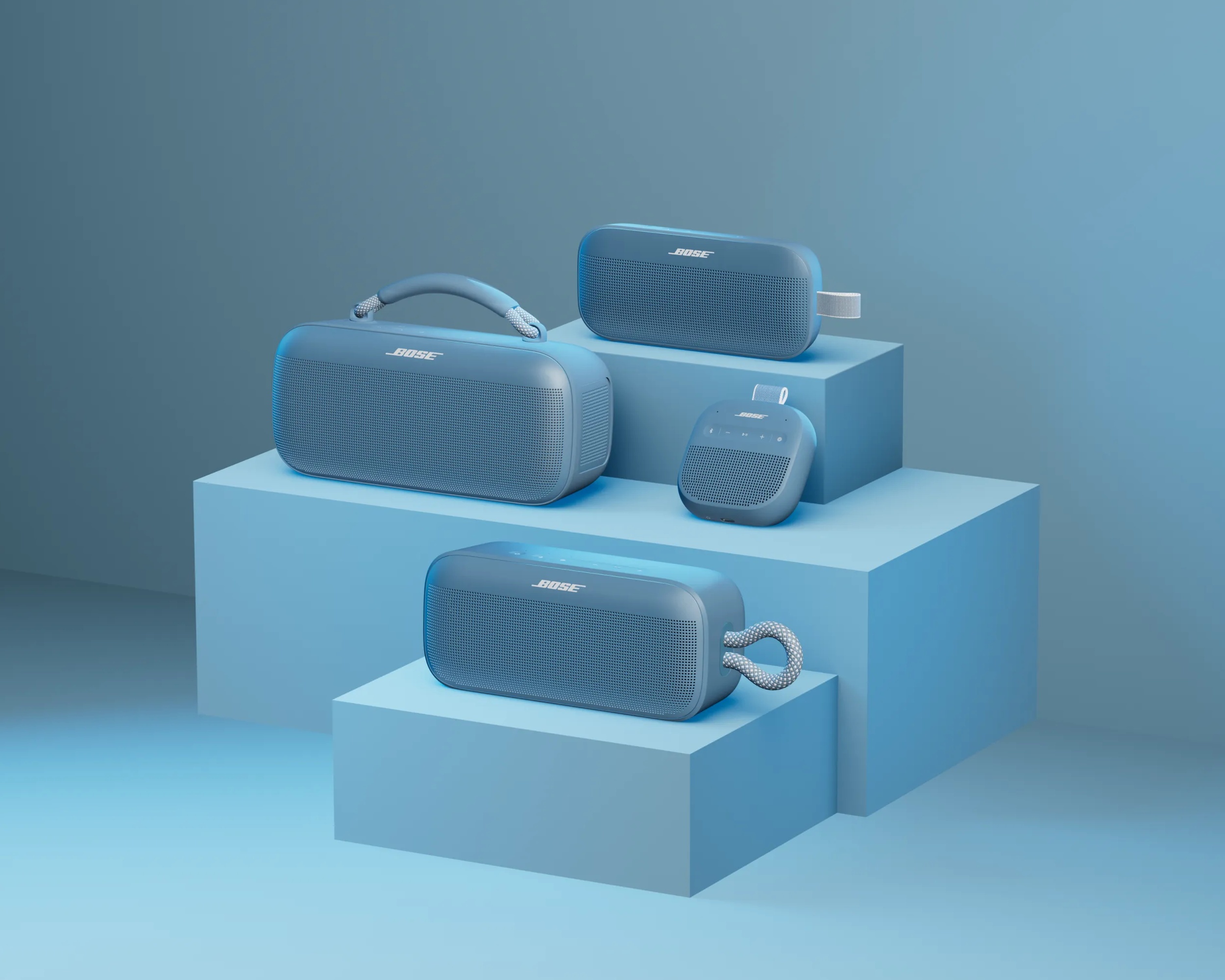 Blue Bose SoundLink Flex Bluetooth Speaker (2nd Gen), SoundLink Max Portable Speaker, SoundLink Micro Bluetooth Speaker (2nd Gen), and SoundLink Plus Portable Speaker displayed on tiered pedestal blocks.