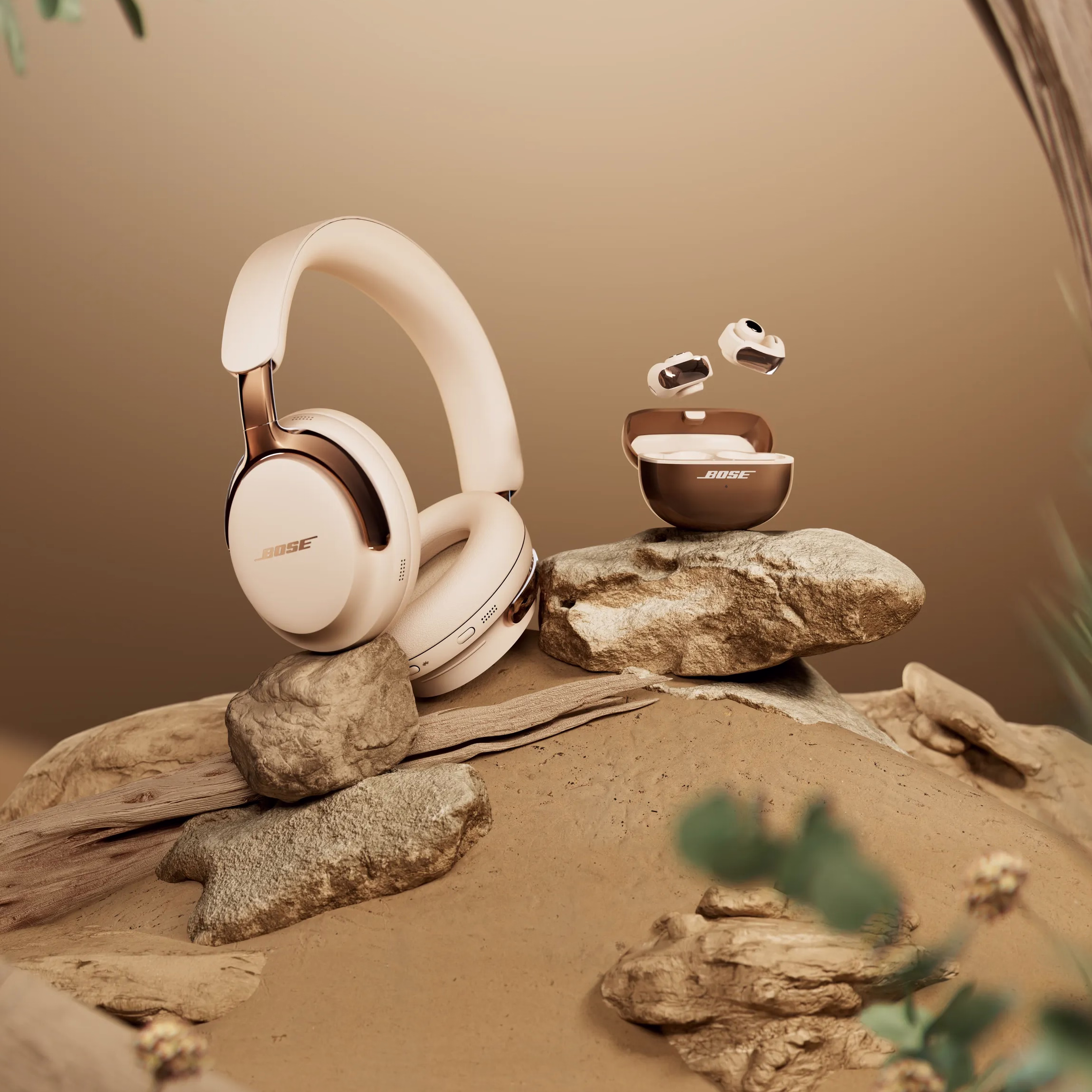 ose QuietComfort Ultra headphones and matching Ultra Open earbuds displayed on natural rocks in a warm, minimalist desert setting with soft lighting and blurred greenery.