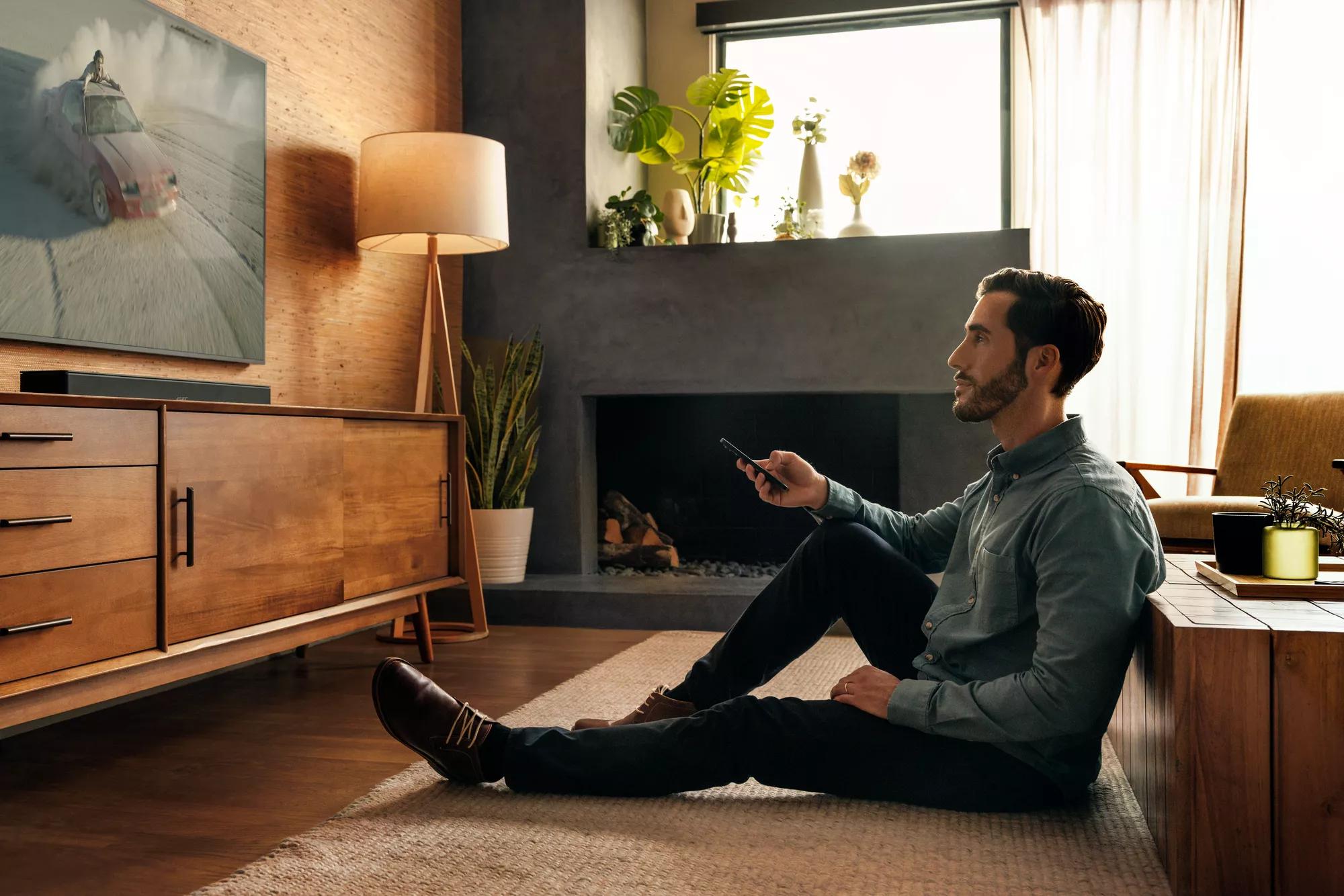 Man sitting on the floor in a living room, watching with a Bose Smart Ultra Soundbar