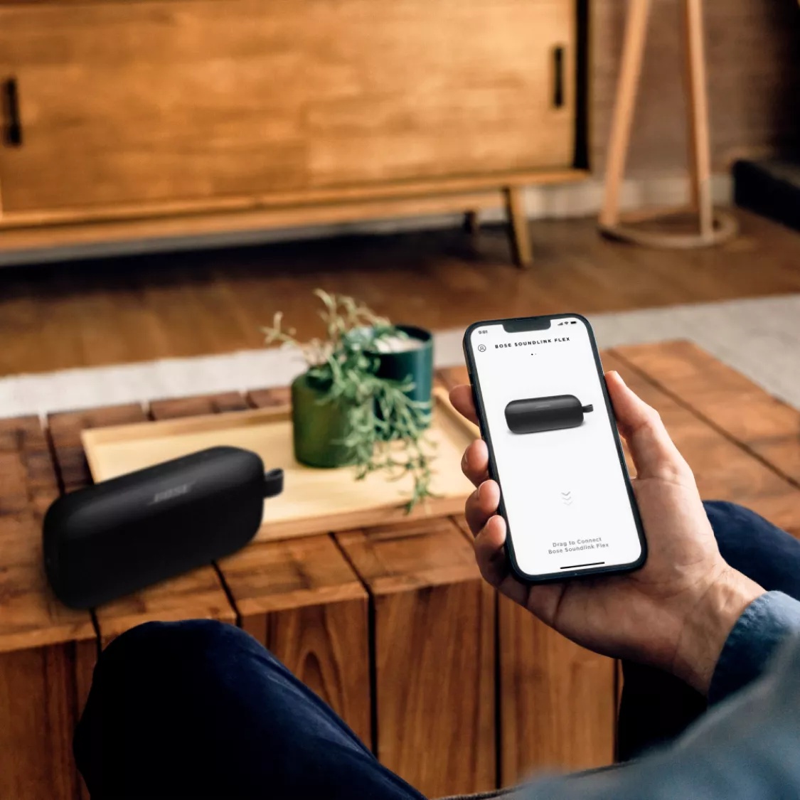 Person sitting in living room connecting Bose SoundLink Flex Speaker with the Bose Music app