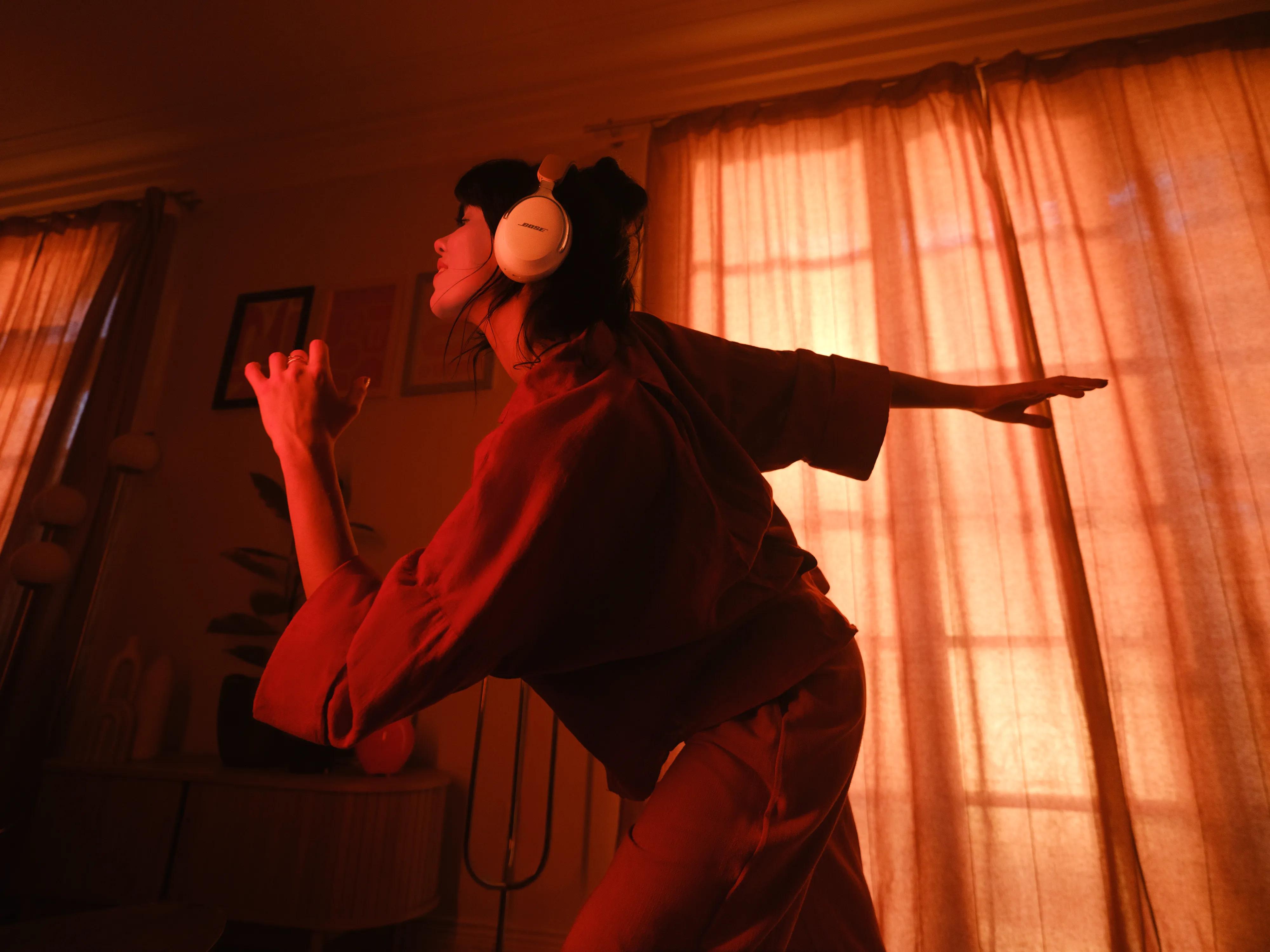 Woman wearing Bose QuietComfort Ultra Headphones (2nd Gen) while stretching in her apartment. 