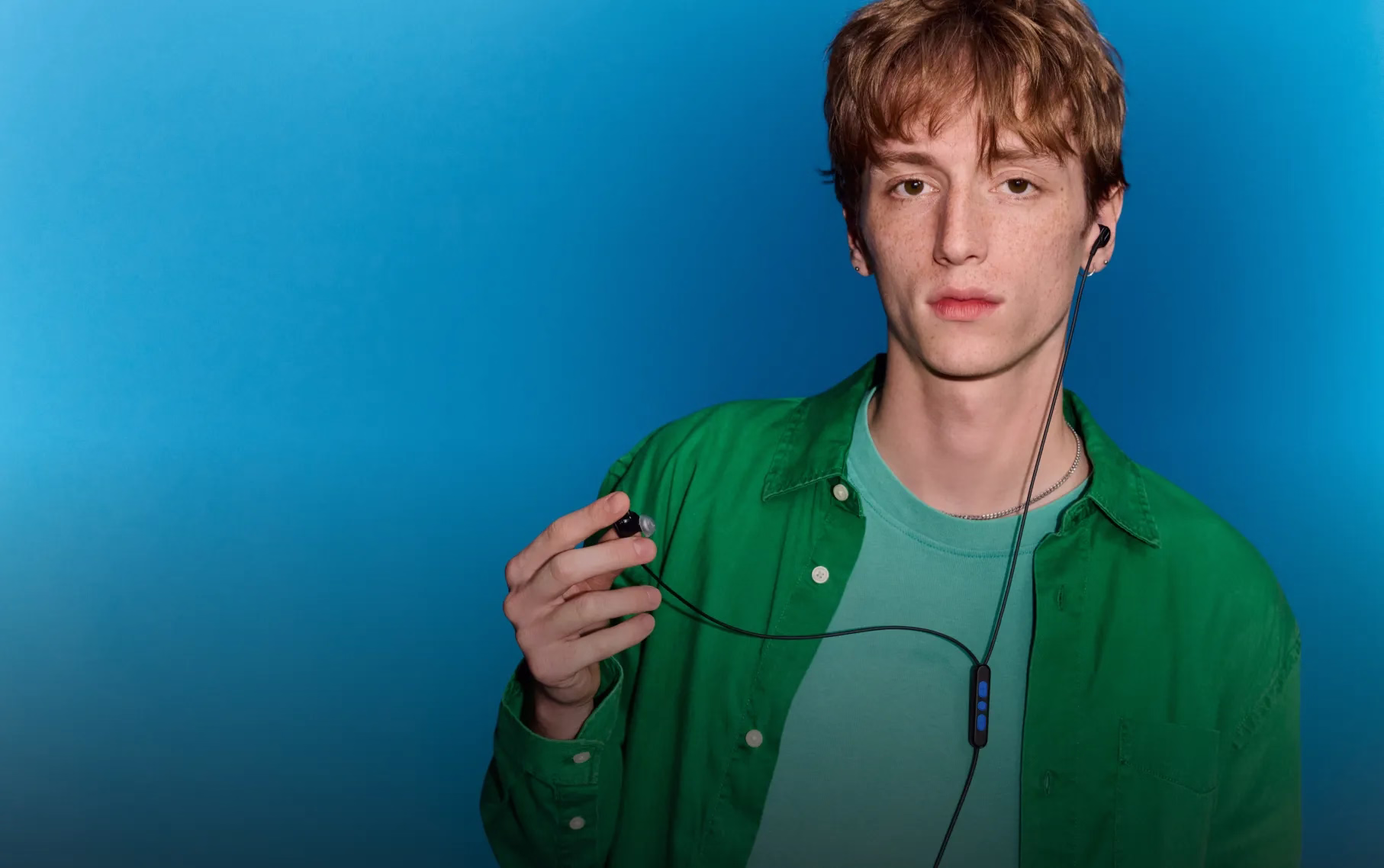 Young man with one earbud of the Bose Noise Cancelling Wired Earbuds in his ear and holding the second earbud in his hand.
