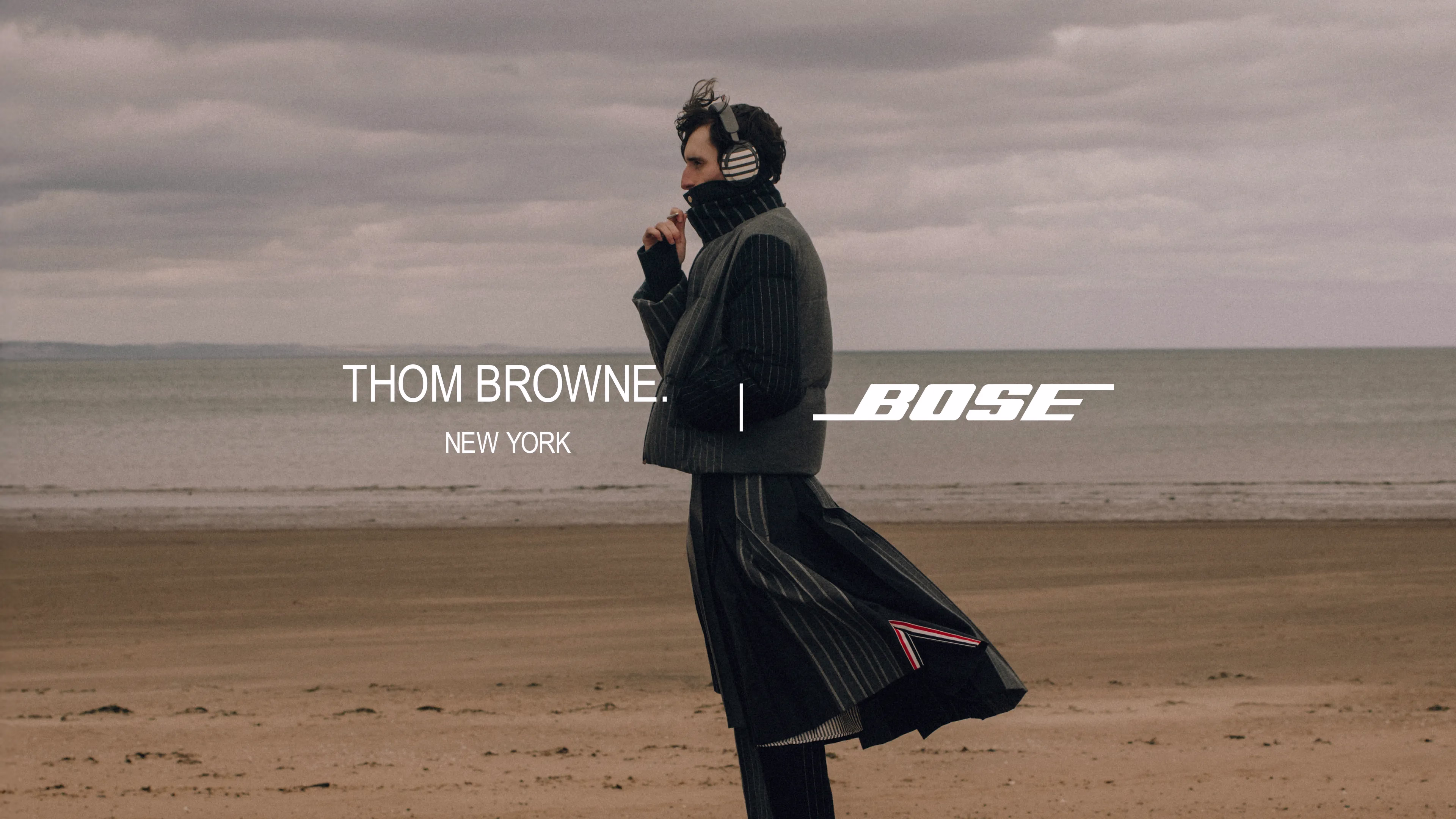 Logo von Bose und Thom Browne sowie ein Mann, der am Strand steht und die Bose &times; Thom Browne QuietComfort Ultra Kopfh&ouml;rer (2. Gen.) tr&auml;gt.