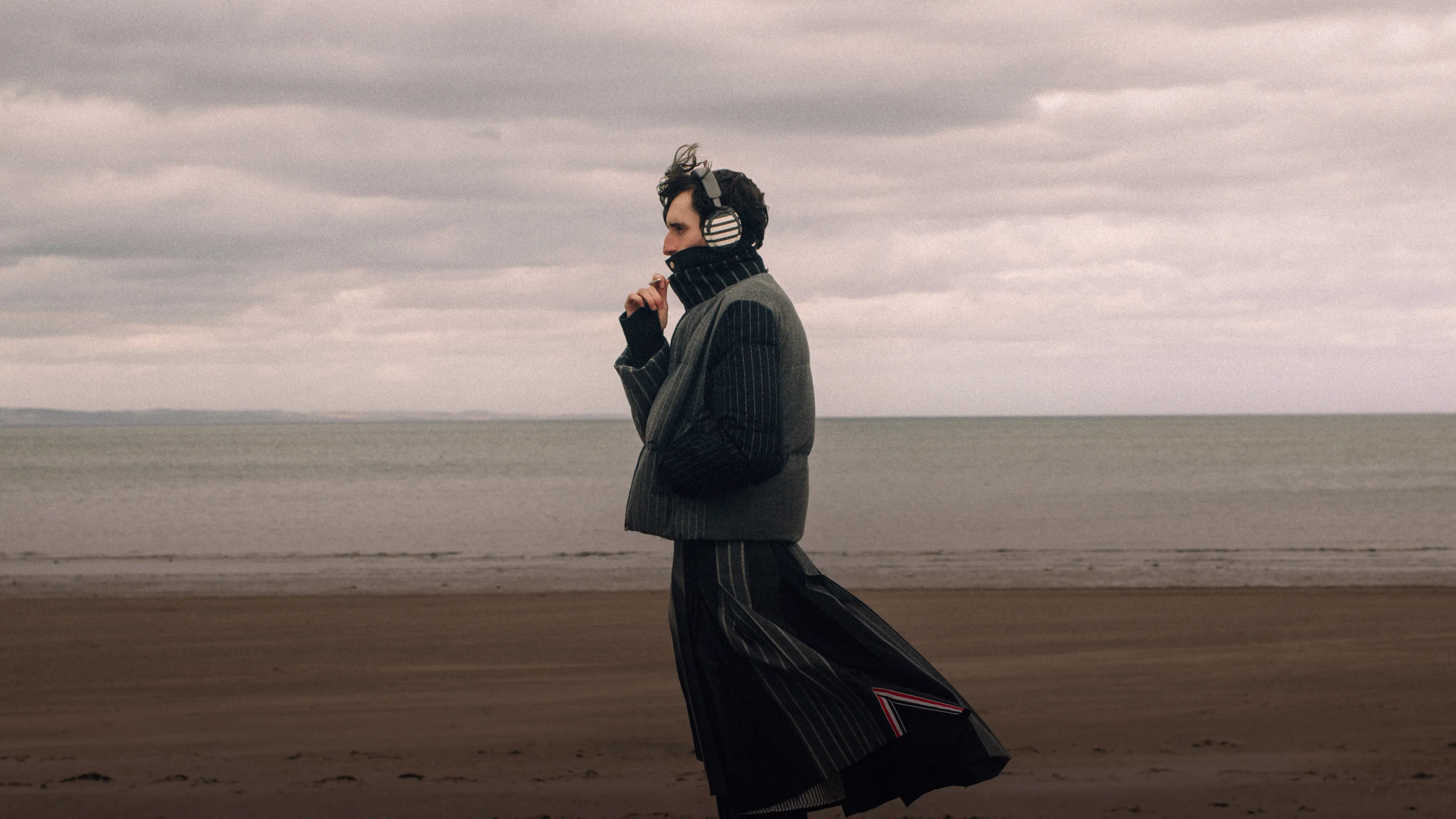 Homme portant le casque QuietComfort Ultra (2e&nbsp;g&eacute;n&eacute;ration) Bose &times; Thom Browne debout sur la plage.