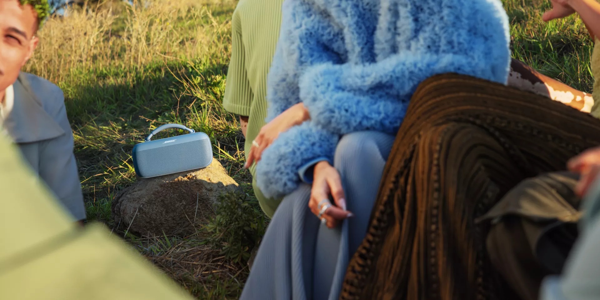 Young people gathered outside listening to music from a Bose SoundLink Max Portable Speaker