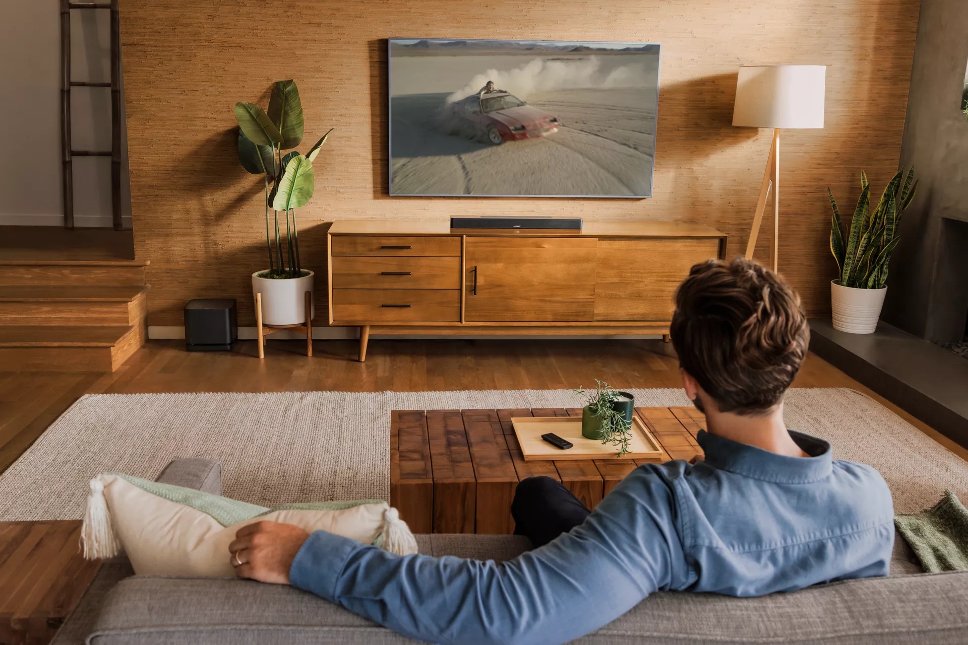 Guy sitting on couch in living room watching a movie with Smart Soundbar 600 and Bass Module 500