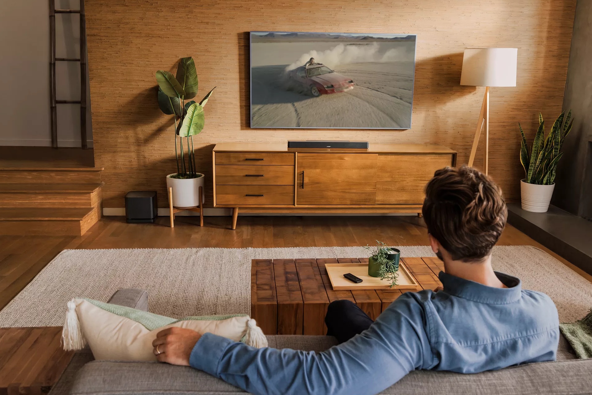 Guy sitting on couch in living room watching a movie with Smart Soundbar 600 and Bass Module 500
