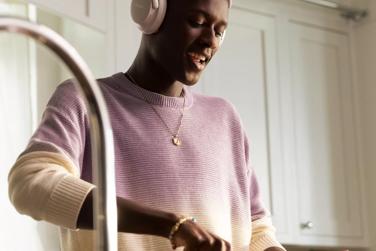 Man standing over sink whisking ingredients in a bowl and wearing QuietComfort Ultra Headphones