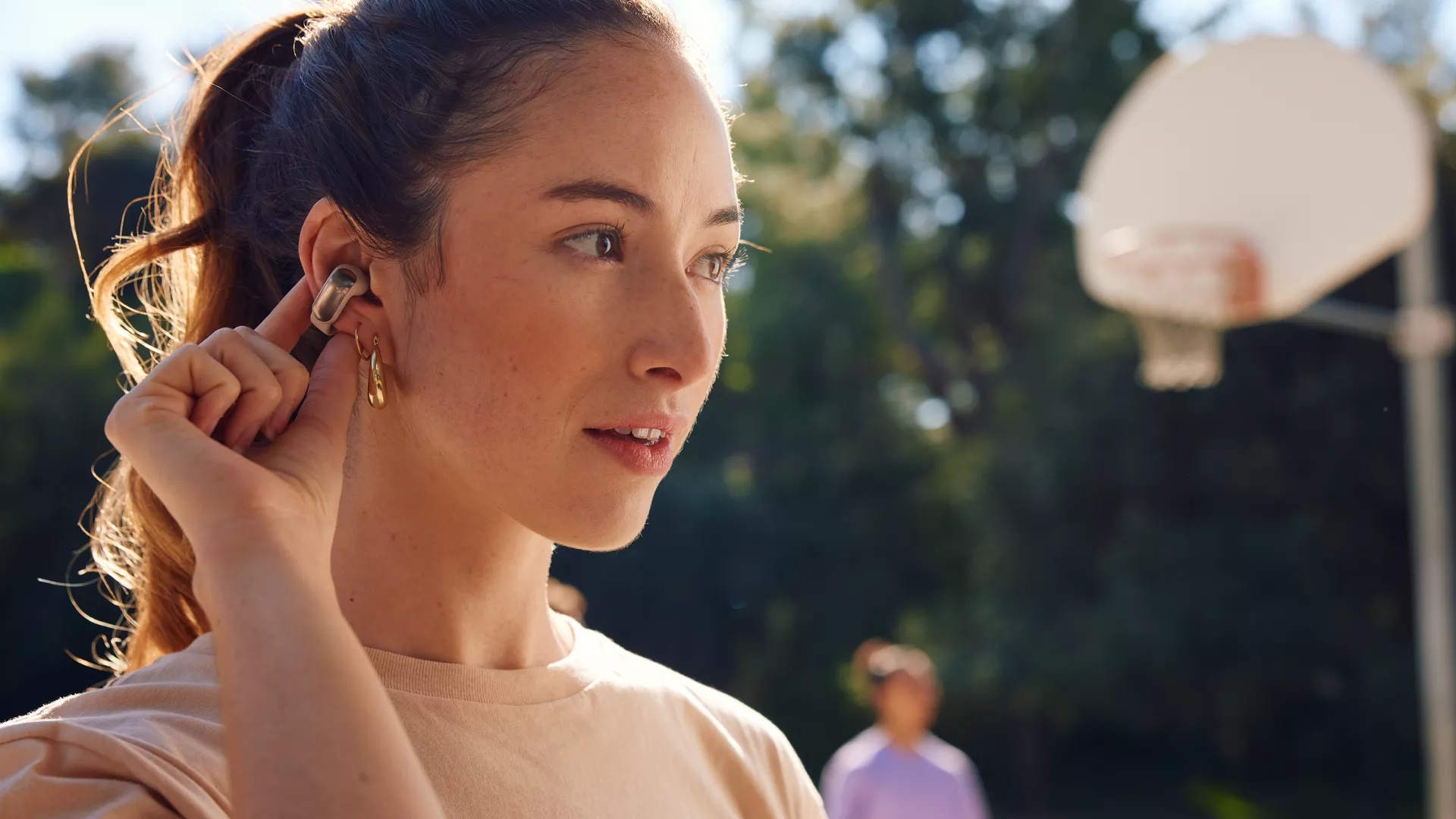 Woman playing basketball and adjusting music on her Bose Ultra Open Earbuds