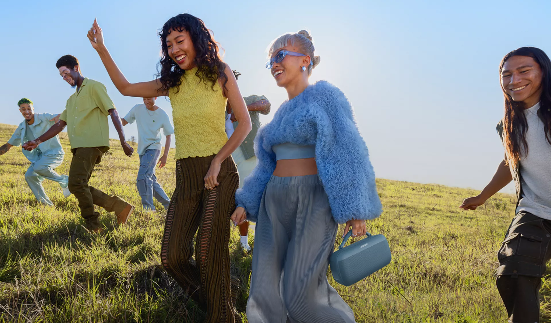 Young people walking across a field listening to a Bose SoundLink Max Portable Speaker 