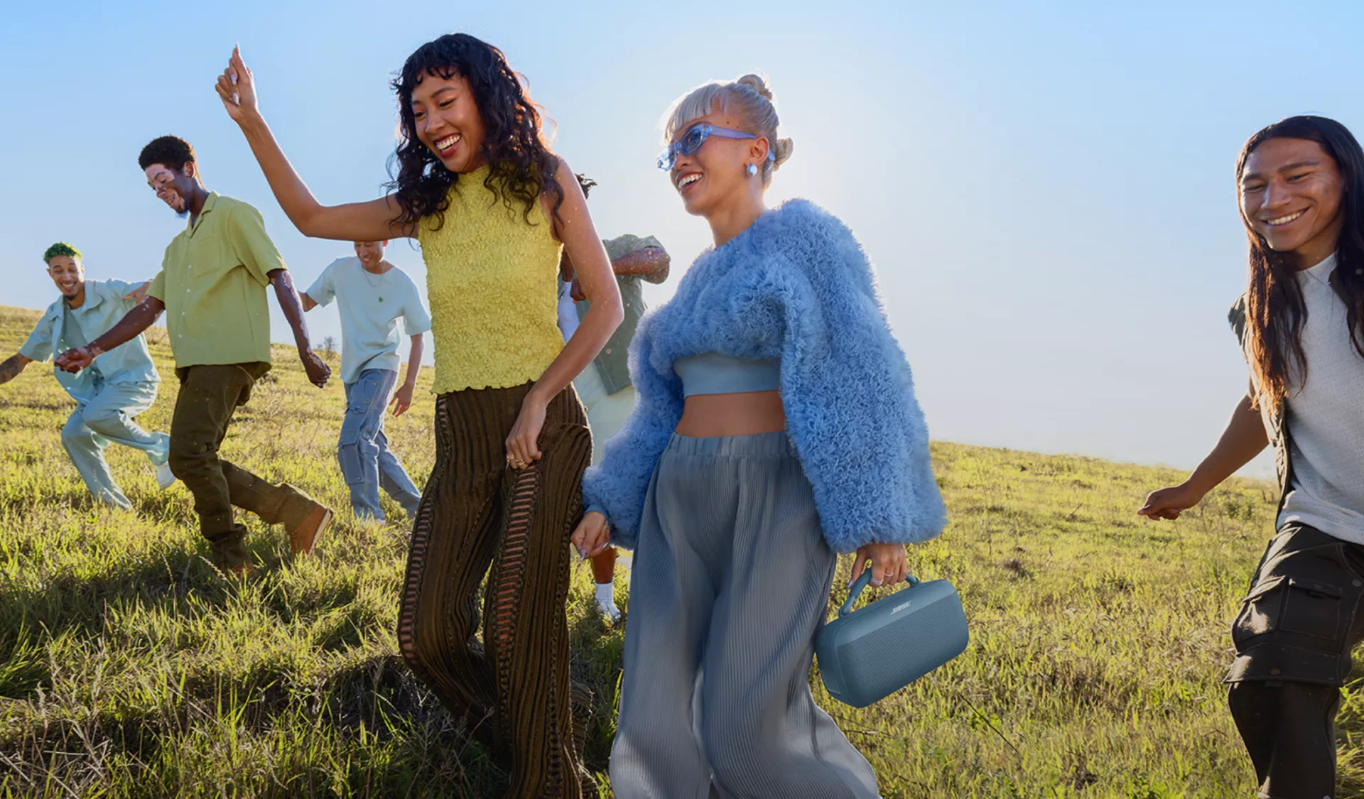 Jóvenes caminando por un campo escuchando un altavoz portátil Bose SoundLink Max 