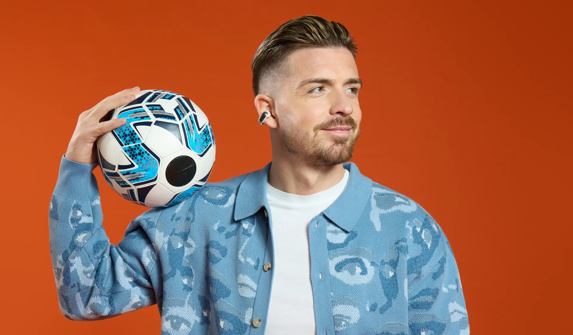 Jack Grealish wearing Bose Ultra Open Earbuds while holding a soccer ball