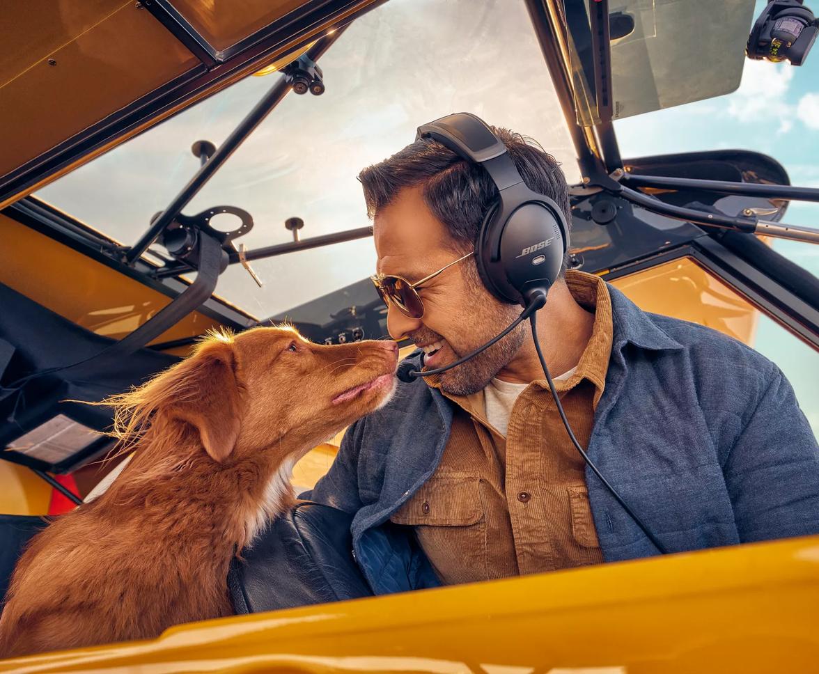 Pilot sitting in a cockpit wearing the Bose A30 Aviation Headset turning to look at his dog