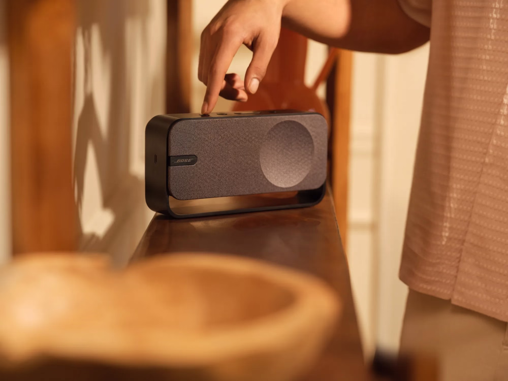 A hand turning on a Bose SoundLink Home standing in a table 
