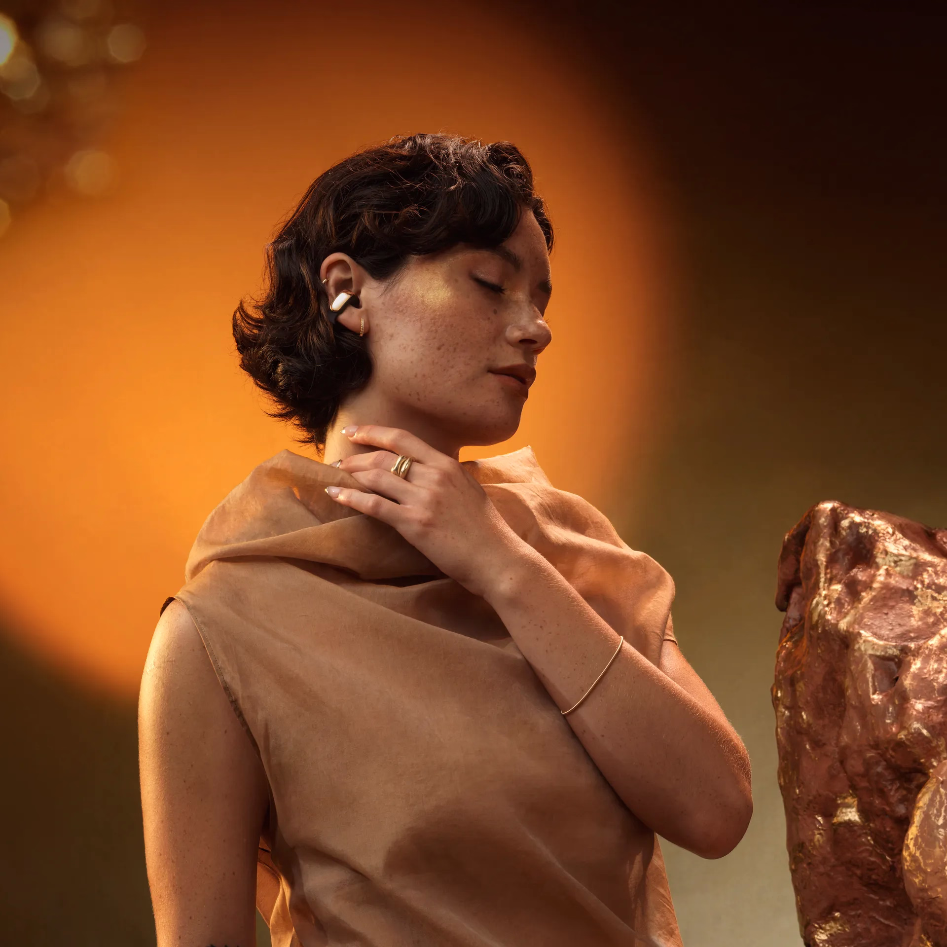 Woman wearing Ultra Open Earbuds LE in Desert Gold, shown in a warm-toned setting with soft lighting, highlighting the open-ear design and elegant metallic finish.