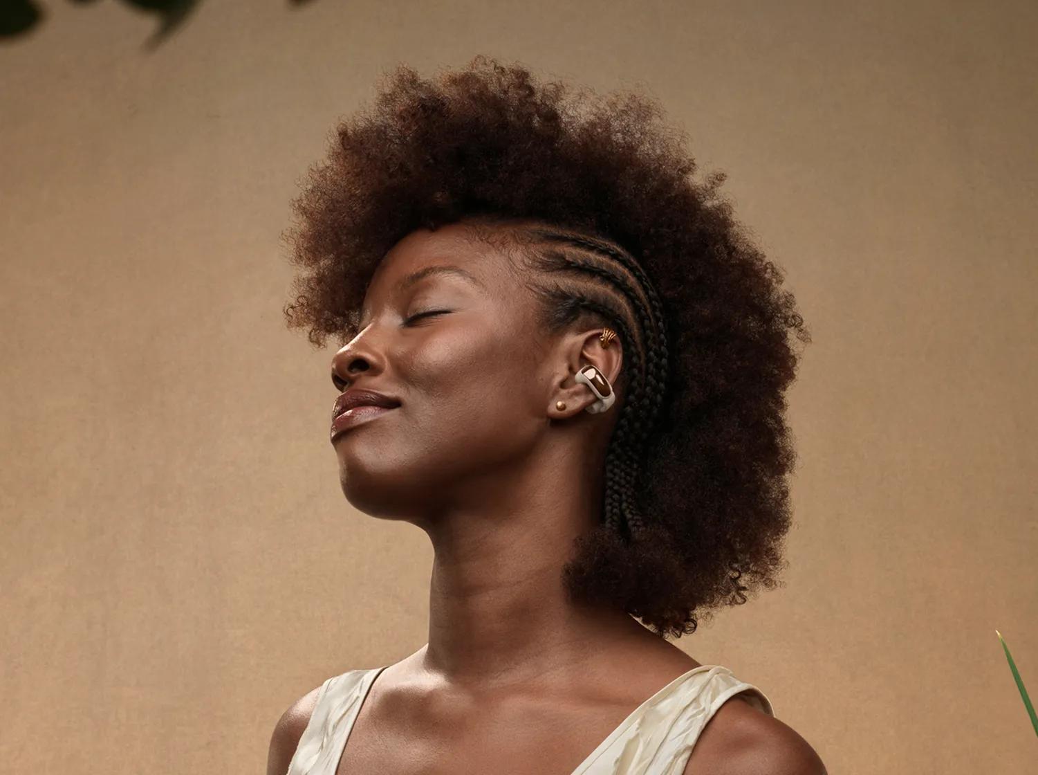 Woman wearing Bose Ultra Open Earbuds in Driftwood Sand.