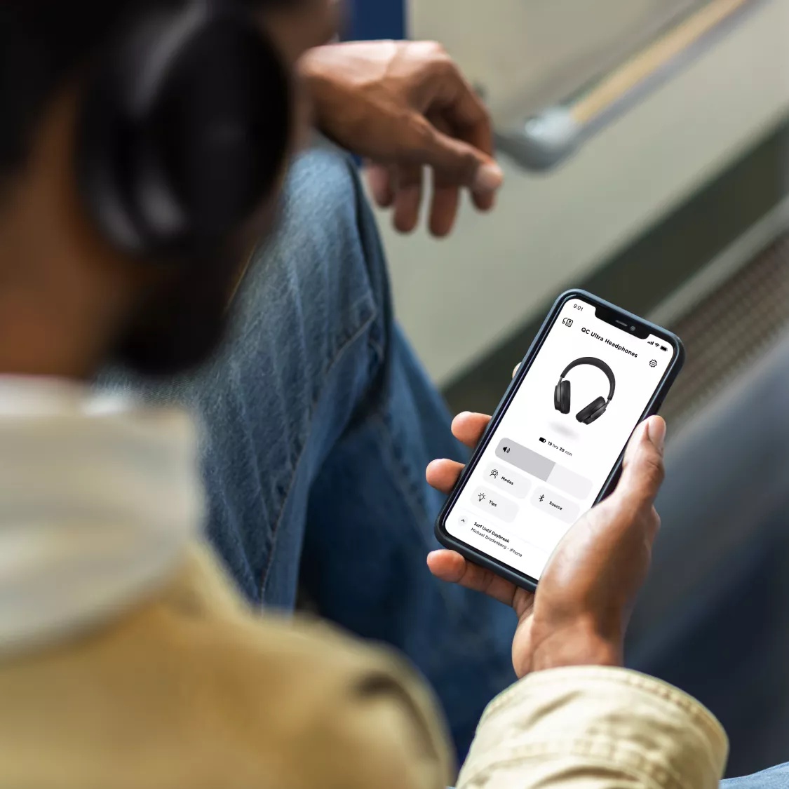 Homme assis dans un train, ajustant la technologie Bluetooth multipoint de son casque QuietComfort Ultra grâce à l’application Bose