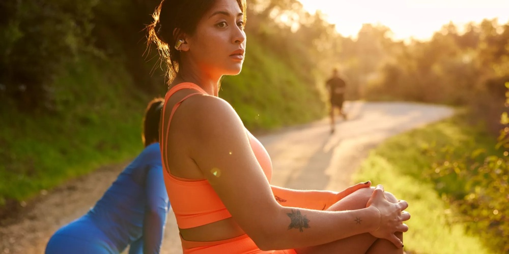 Une femme portant des écouteurs oreilles libres Bose Ultra en train de faire des étirements avant d’aller courir