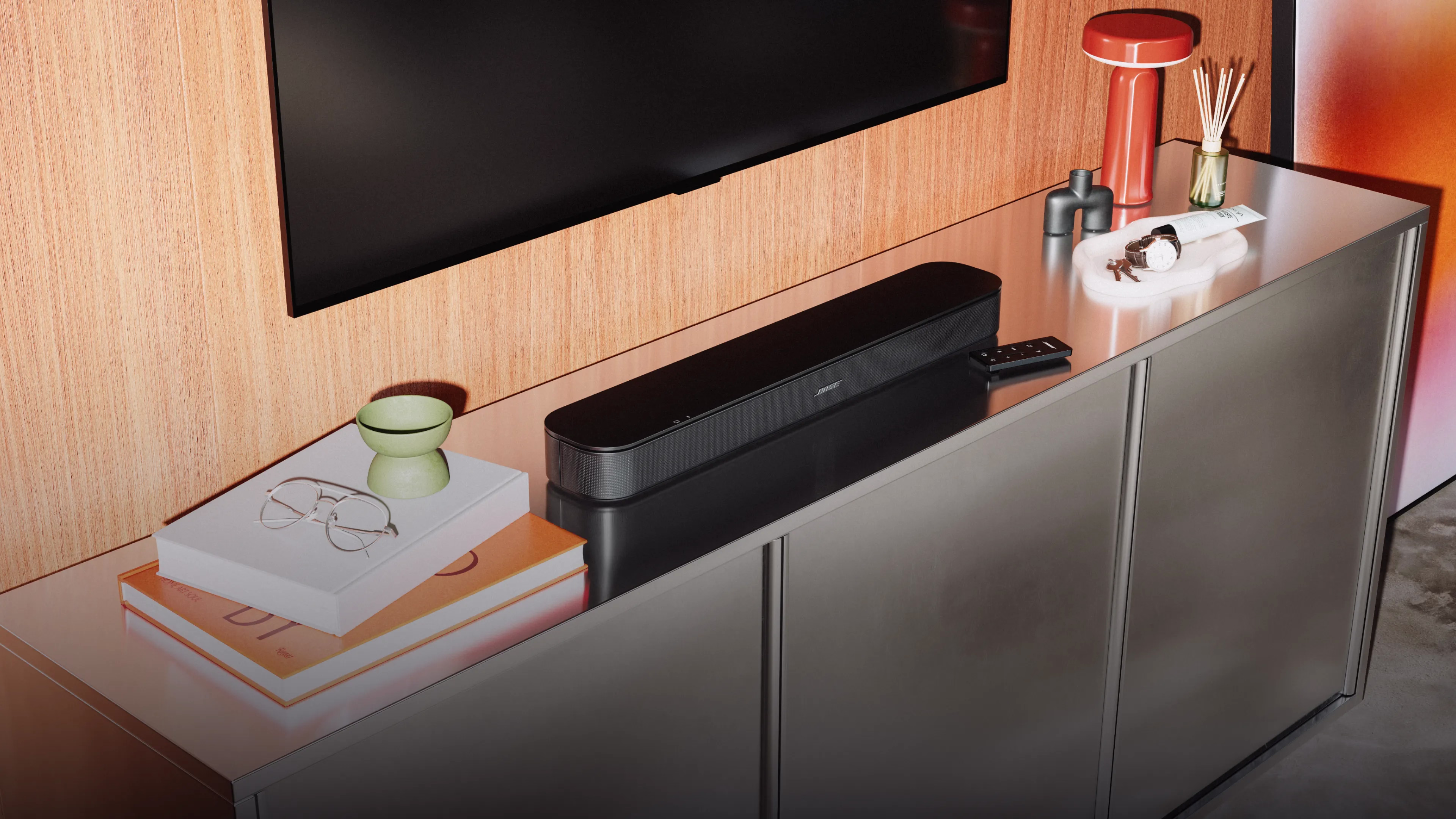 Bose TV Speaker (2nd Gen) and its remote on a TV console with a TV mounted on the wall above them.
