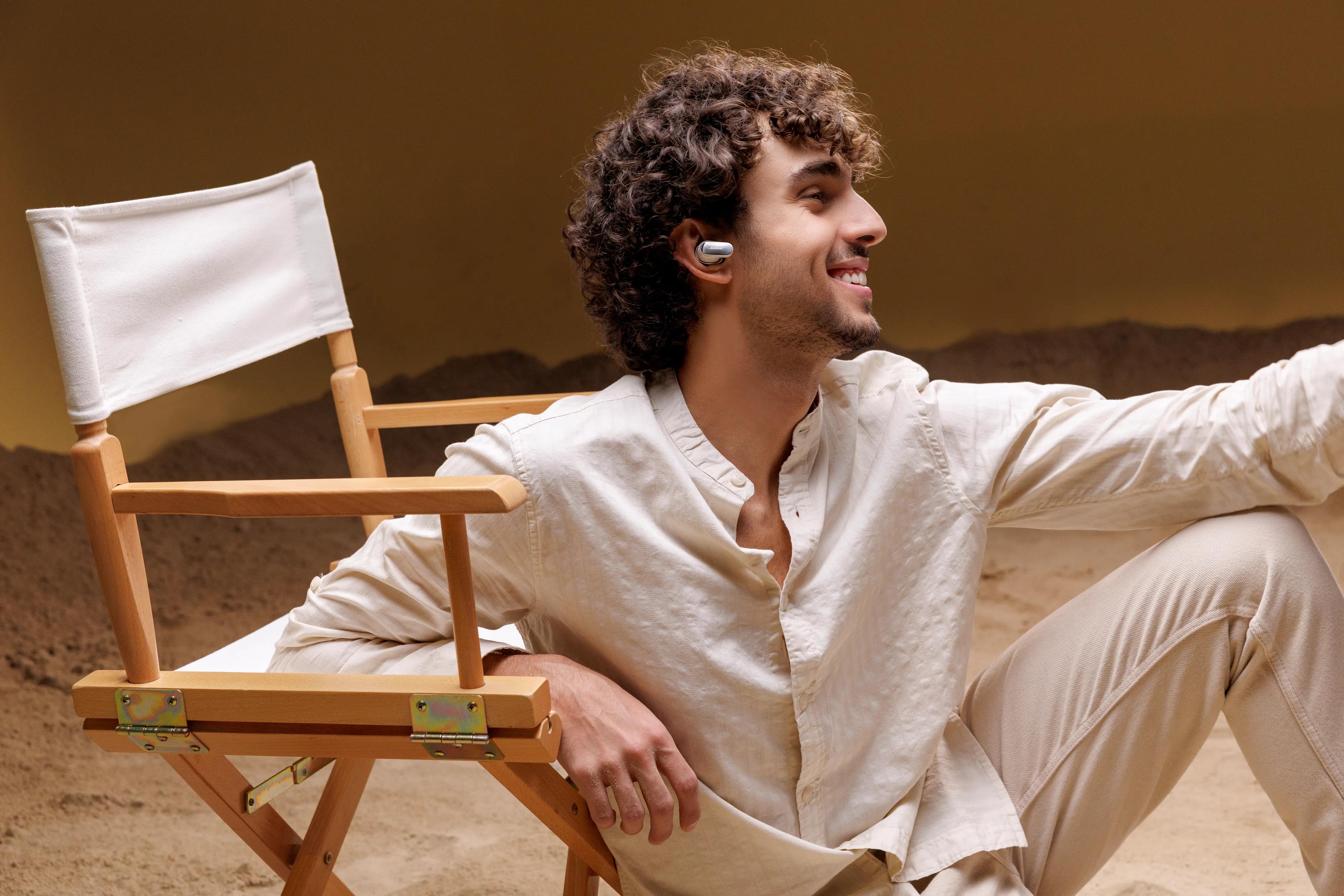 Man wearing Bose QuietComfort Ultra Earbuds (2nd Gen).while sitting on the floor leaning against a chair.