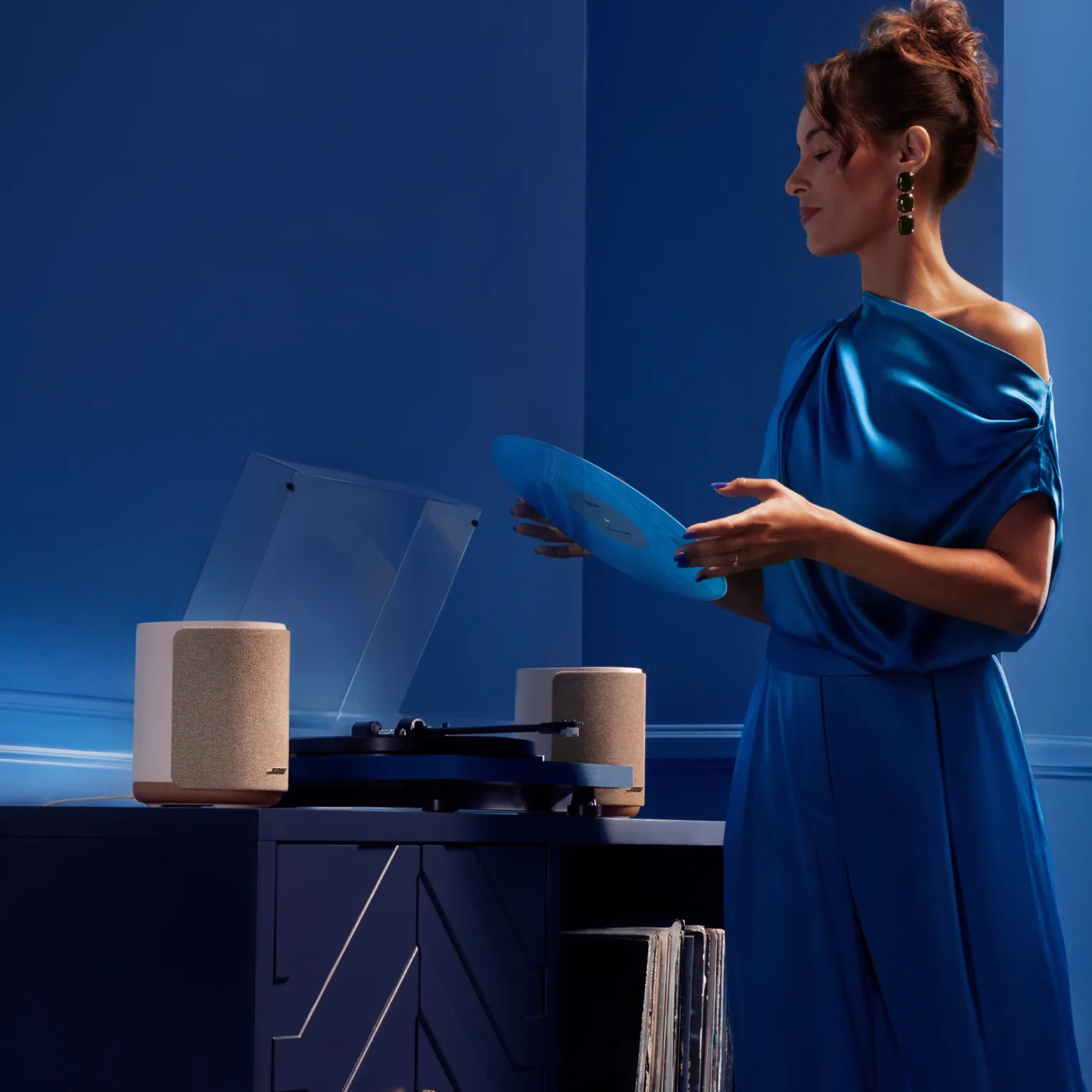 レコードアルバムをターンテーブルにセットする女性。ターンテーブルにはBose Lifestyle Ultra Speakerが2台接続されている。