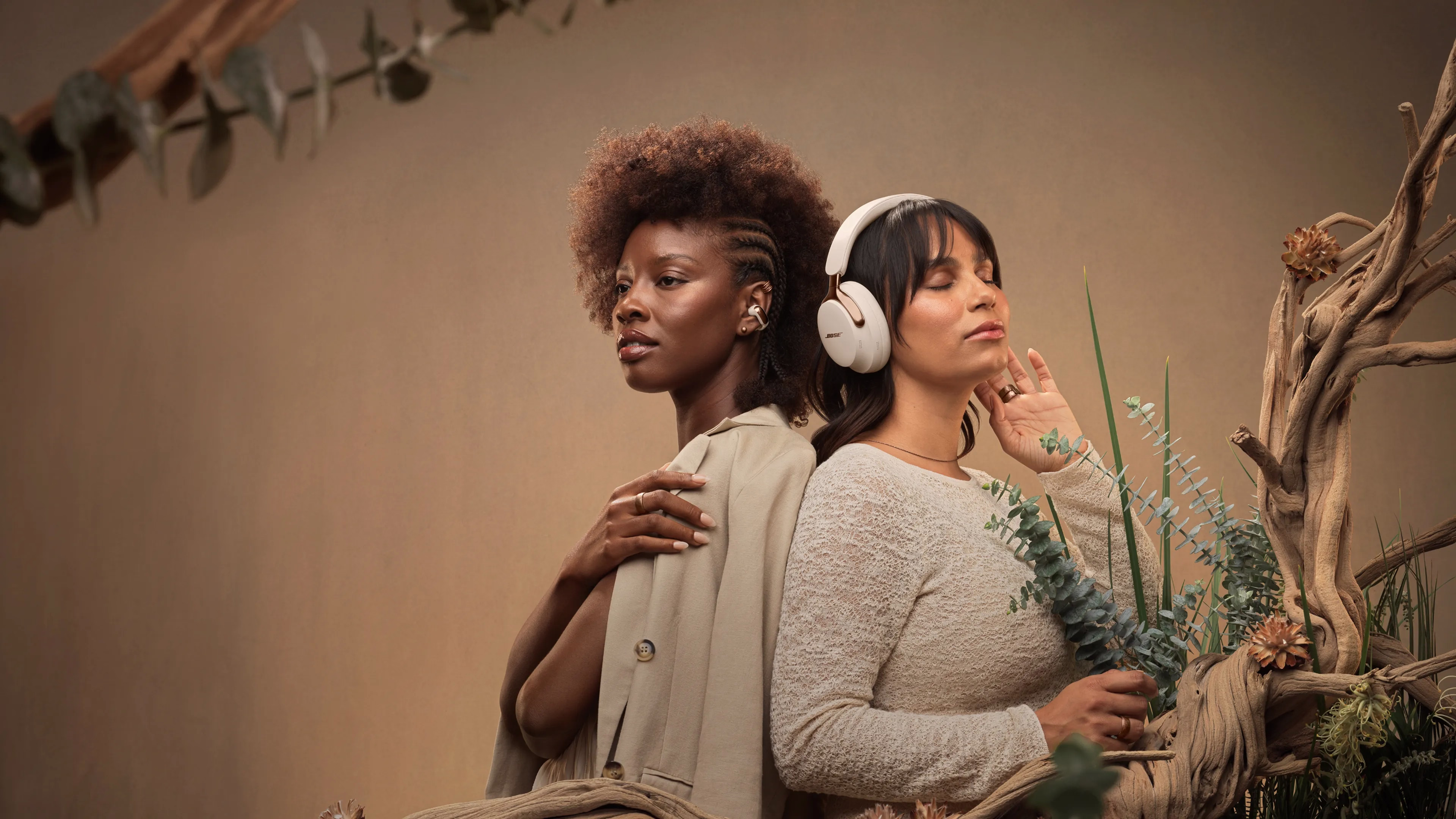 Woman wearing Bose Ultra Open Earbuds and another woman wearing QuietComfort Ultra Headphones, both is Driftwood Sand.