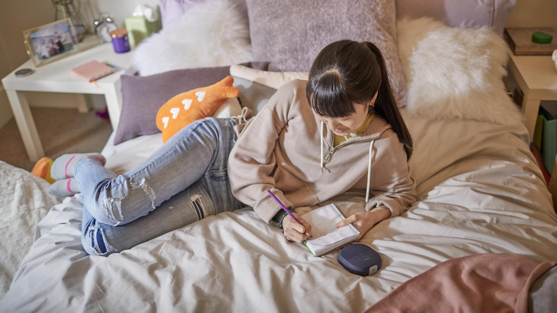 Young woman listening to music from a SoundLink Micro Bluetooth Speaker while lying on her bed