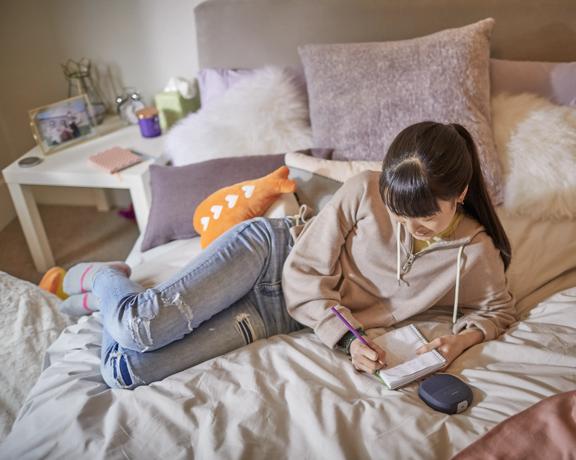 Young woman listening to music from a SoundLink Micro Bluetooth Speaker while lying on her bed