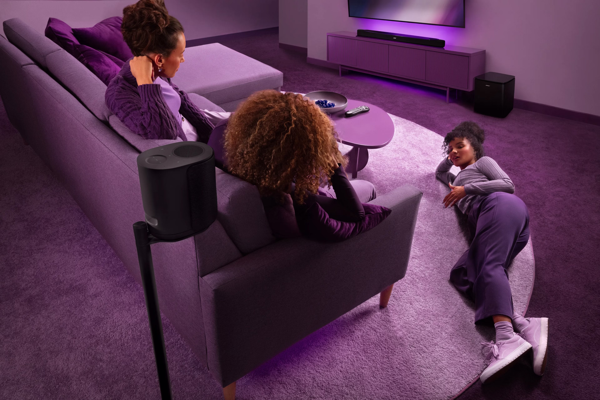 Lifestyle Ultra home theater system featuring the Lifestyle Ultra Speaker on a Floor Stand, Lifestyle Ultra Soundbar, Lifestyle Ultra Speaker surrounds, and Lifestyle Ultra Subwoofer, creating an immersive surround sound experience in a modern living room with people enjoying.