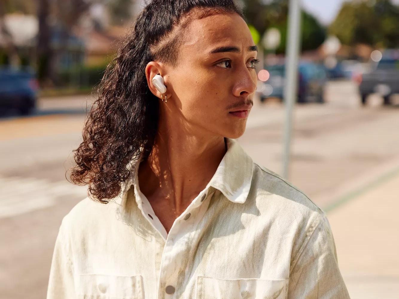 Young man walking down a street, holding his phone, and listening to music through his Bose QuietComfort Ultra Earbuds