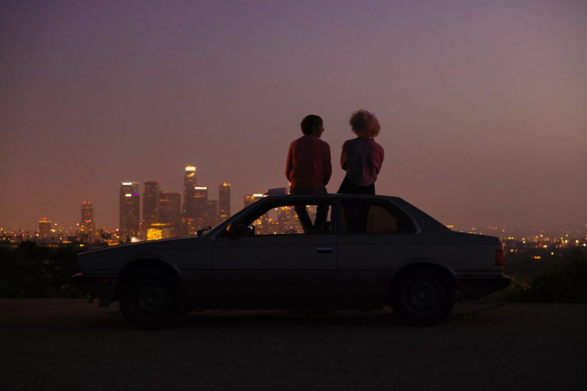 Couple assis sur le toit d’une voiture admirant la silhouette de la ville et écoutant une enceinte Bluetooth Bose SoundLink Flex