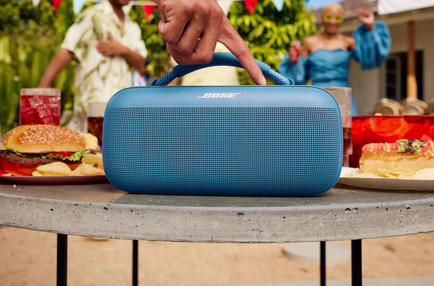 Person pressing ‘Play’ on a Bose SoundLink Max Portable Speaker at a backyard barbecue