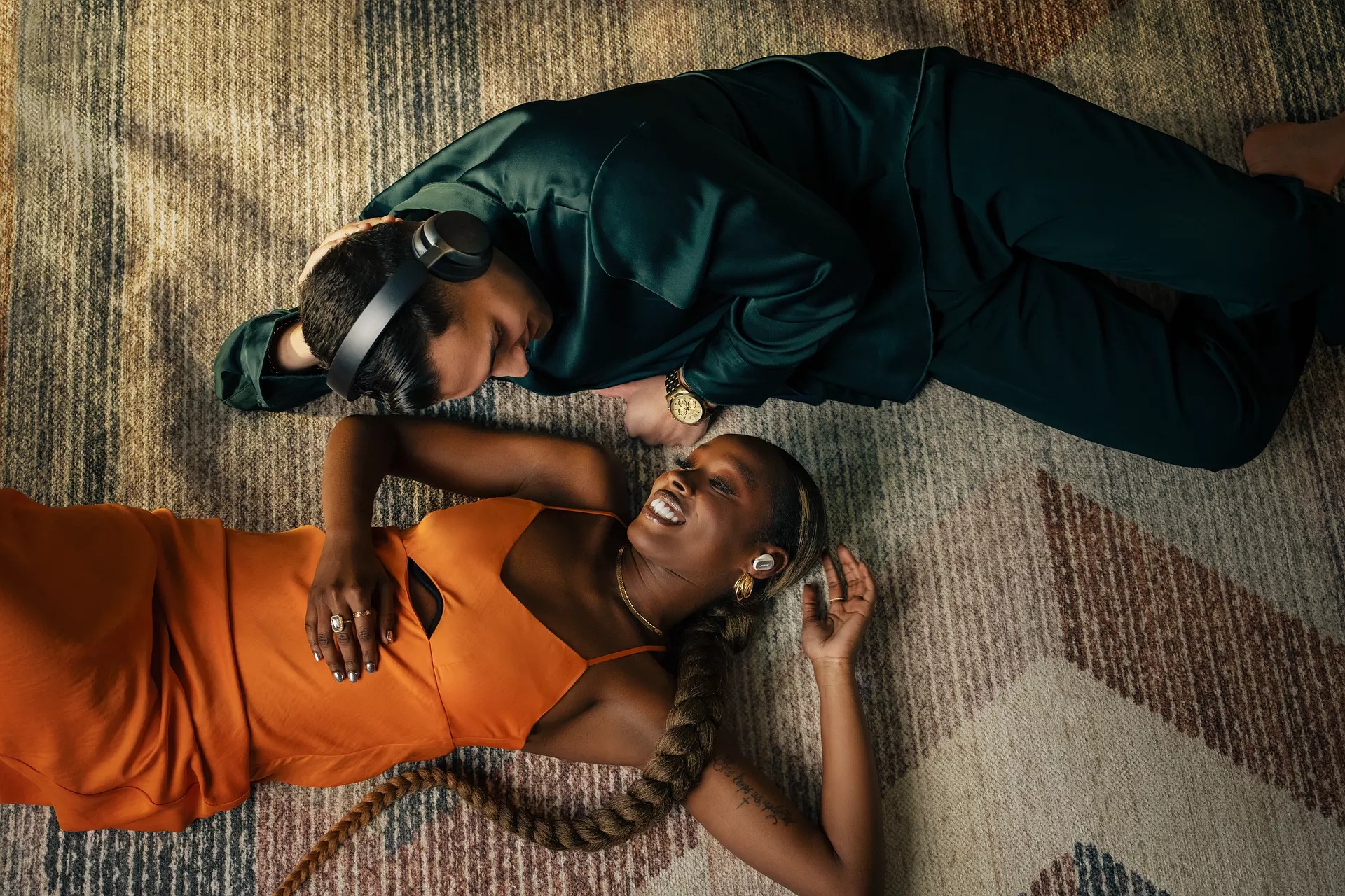 Un couple couché sur un tapis en portant des écouteurs et un casque QuietComfort Ultra sans fils entremêlés