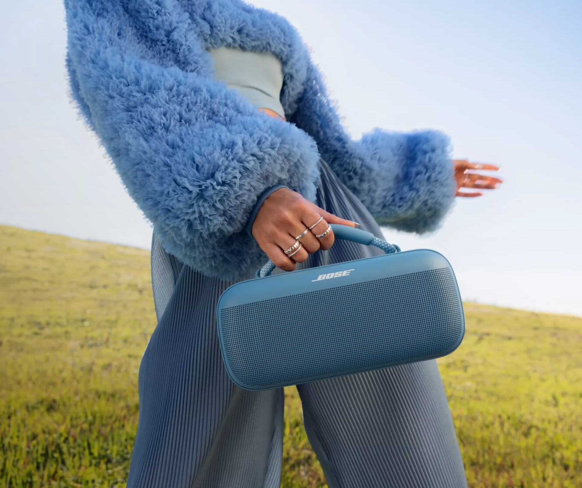 Young woman carrying a Bose SoundLink Max Portable Speaker through a field