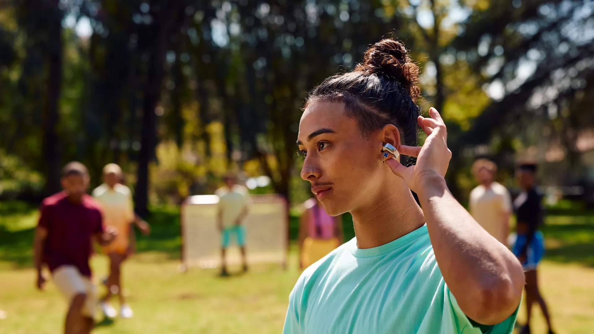 Young man listening to music, using the touch controls of the Bose Ultra Open Earbuds while playing soccer