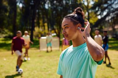 Young man listening to music, using the touch controls of the Bose Ultra Open Earbuds while playing soccer