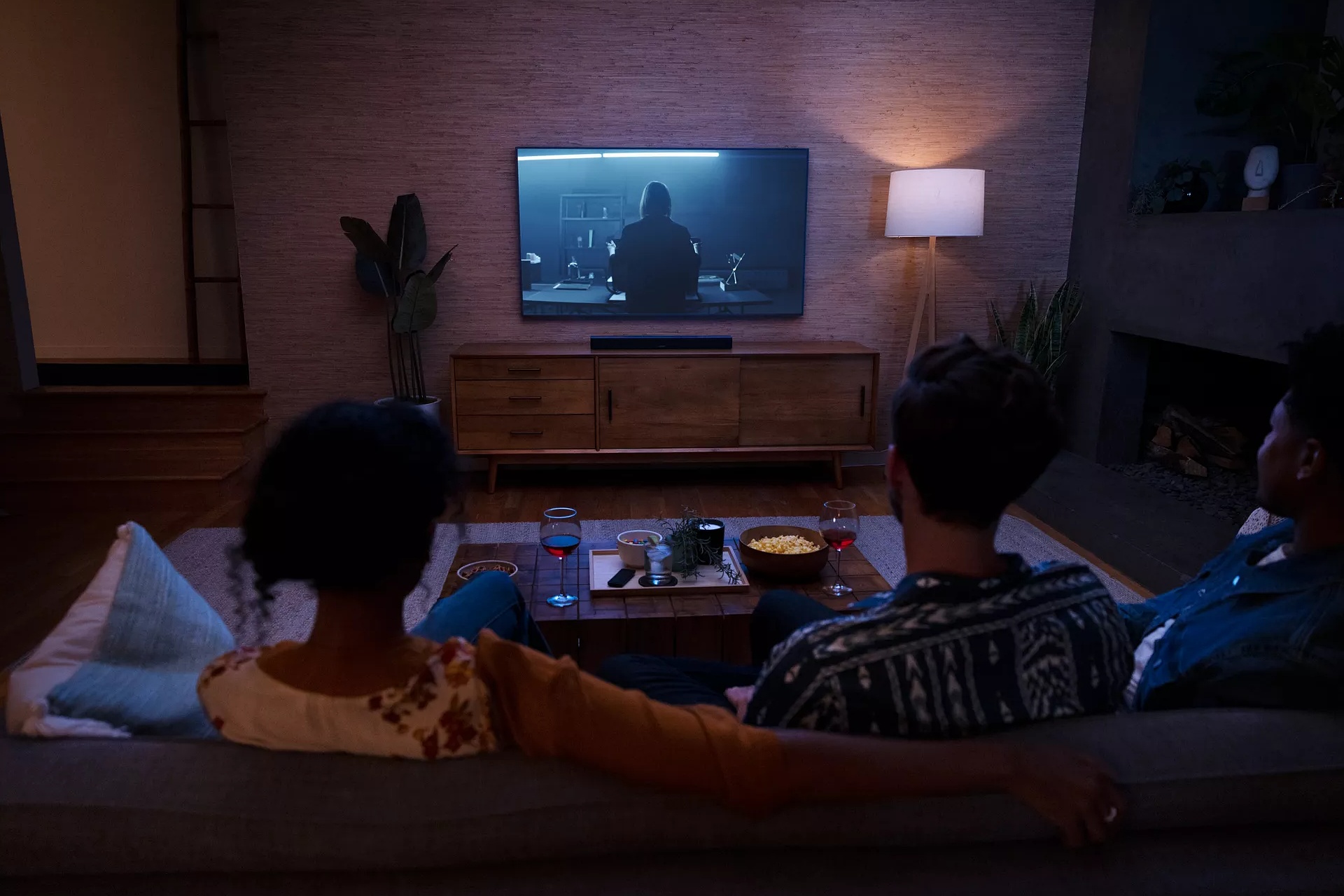 Groupe d’amis assis sur un canapé, buvant du vin, mangeant du maïs soufflé et regardant un film avec Dolby Atmos depuis une barre de son Bose.