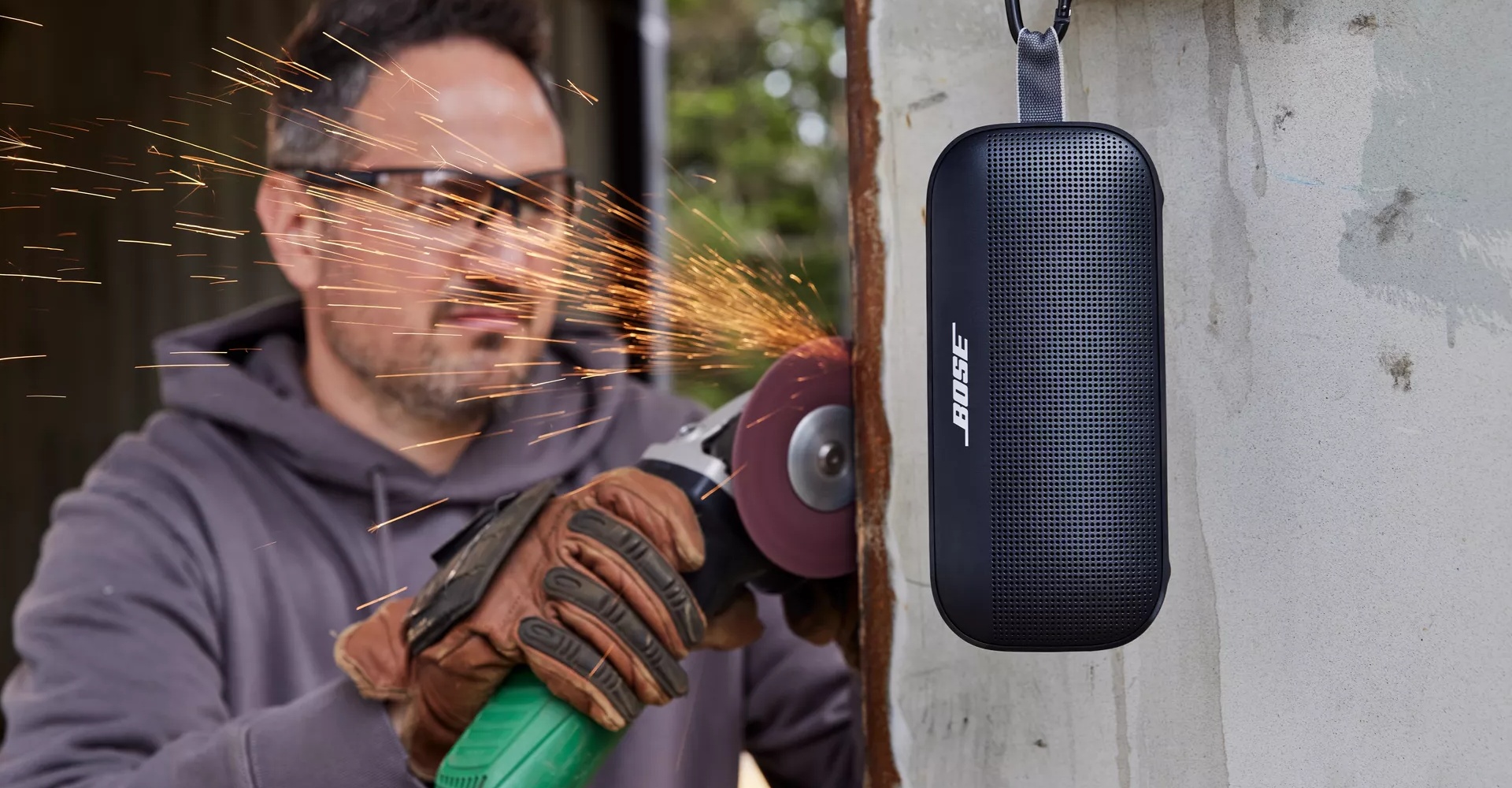 A man working outside with his Bose SoundLink Flex Bluetooth Speaker hanging by the utility loop 
