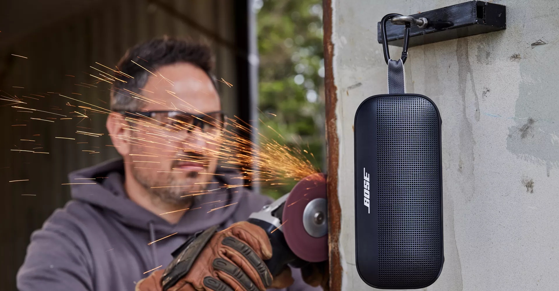 A man working outside with his Bose SoundLink Flex Bluetooth Speaker hanging by the utility loop 