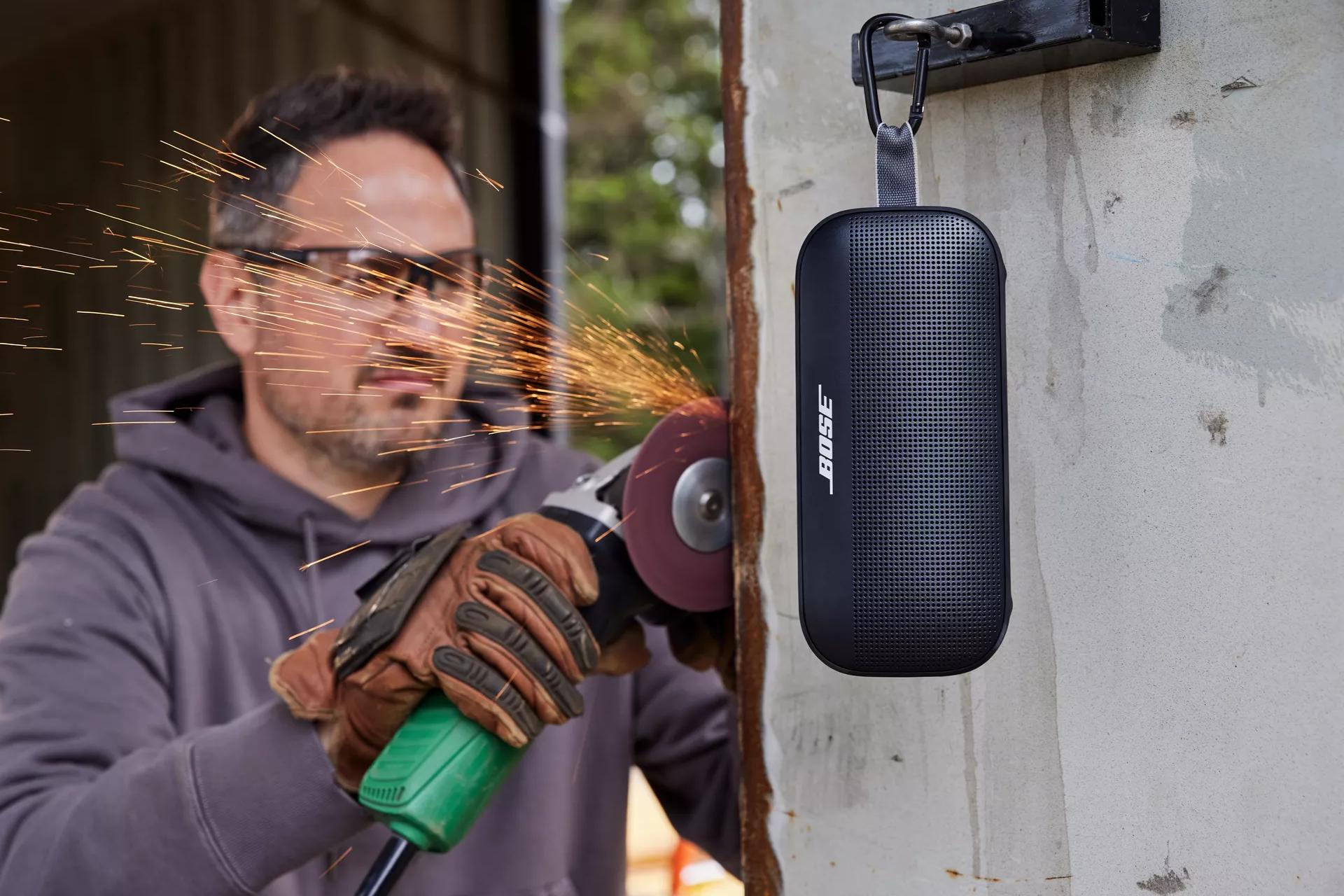 A man working outside with his Bose SoundLink Flex Bluetooth Speaker hanging by the utility loop 