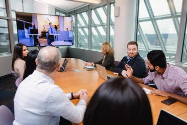 Réunion de collègues dans une salle de conférence avec des participants à distance sur un écran de télévision.