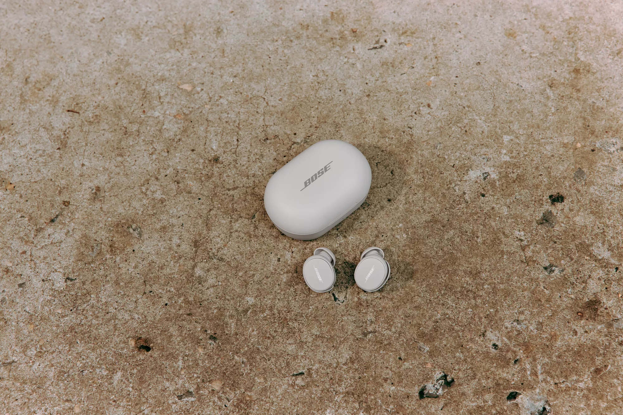 Bose QuietComfort Earbuds and their charging case on a rock.