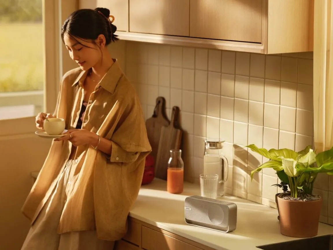 Femme prenant un café dans sa cuisine en écoutant une enceinte Bluetooth Bose SoundLink Home.