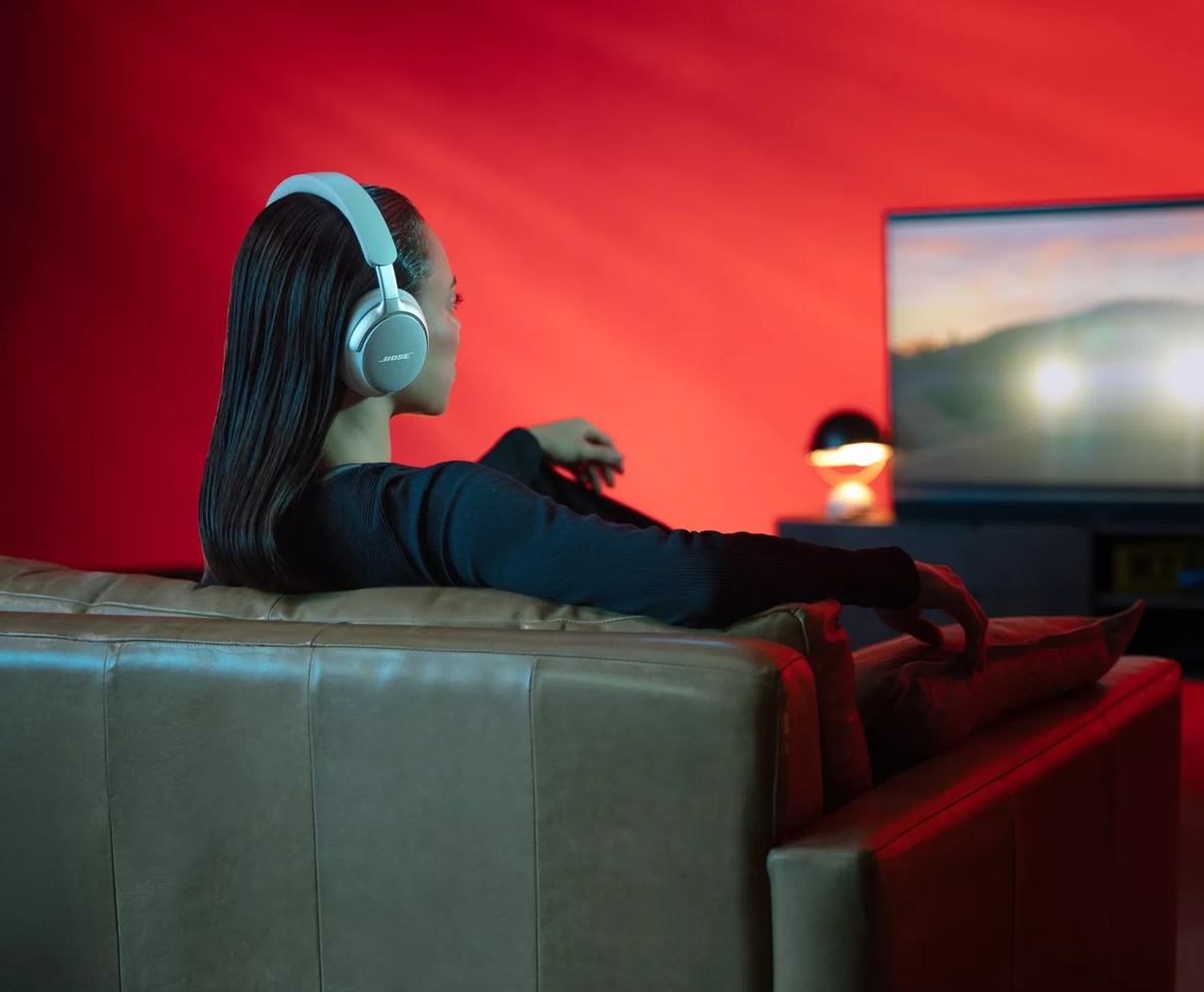 Woman watching TV wearing Bose QuietComfort Ultra Headphones, using SimpleSync with a Bose soundbar.