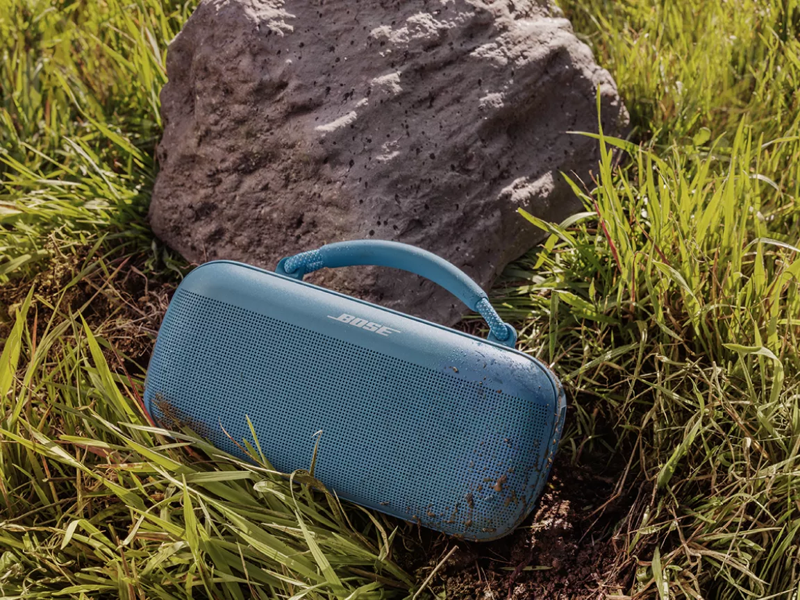 Enceinte portative Bose SoundLink Max sur de l’herbe appuyée contre un rocher